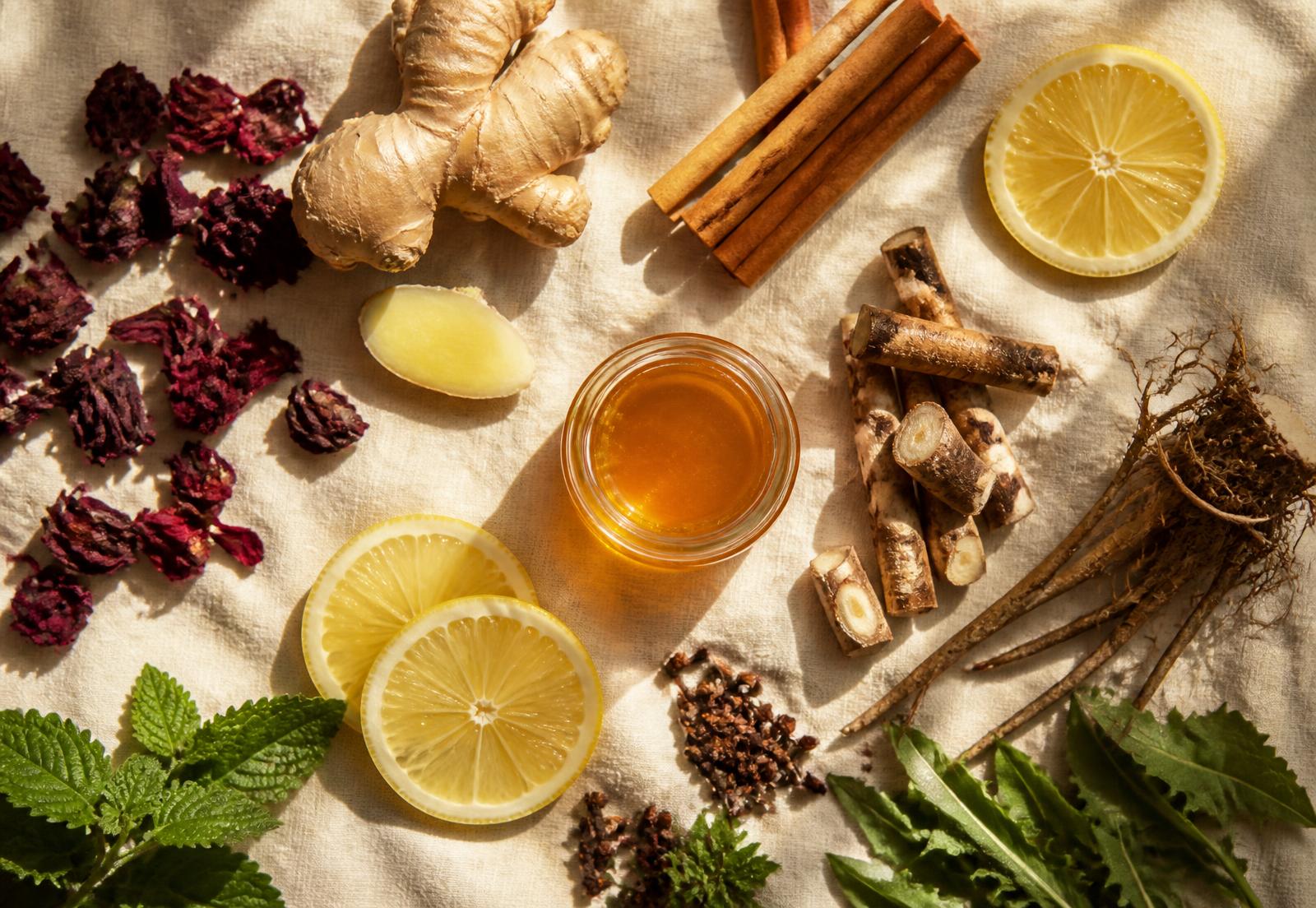 Hibiscus petals, ginger, cinnamon, citrus, roots and raw honey laid out on linen